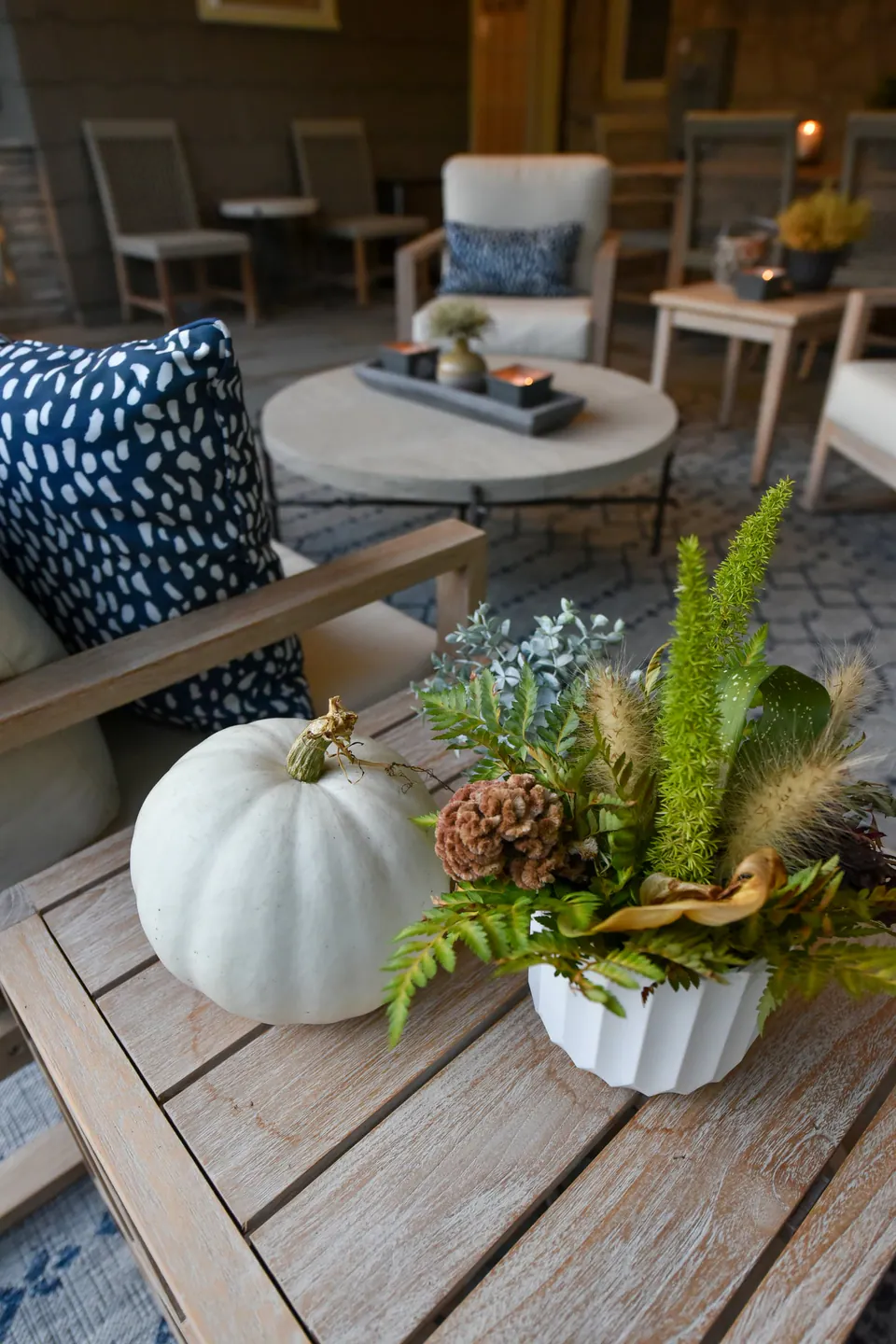 Close patio table detail with white pumpkin, fern, pillows, covered seating, and paver floor